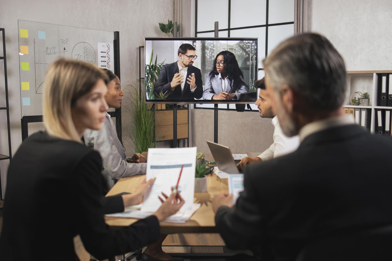 Colleagues in a meeting room watching a video presentation on a wall-mounted screen